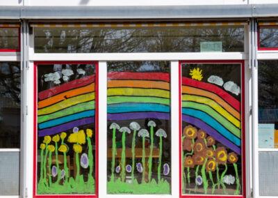 InKiTa Kindergarten Fenstergestaltung mit riesigem Regenbogen und Pilzen und Blumen
